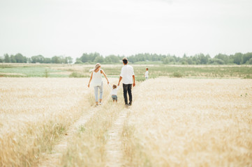 Happy family walking on the path in wheat field at the day time. Concept of friendly family.