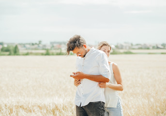 Handsome man is talking on smartphone seriously while standing with the young wife in wheat field on sunny day.