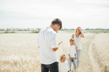 Young father watching something on smart phone strolling together with family on a wheat field.