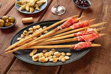Italian antipasti. Grissini with parma ham and roasted almonds, with olives and artichokes, on a dark rustic wooden background
