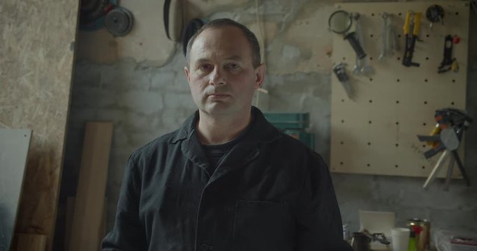 Senior male professional carpentry master standing at wood manufacture turns to camera being calm.