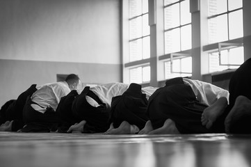 Black and white image of aikido. Men are sporsmen. Aikido workshop. A number of black belt practitioners in traditional uniform, white kimano and black hakama.