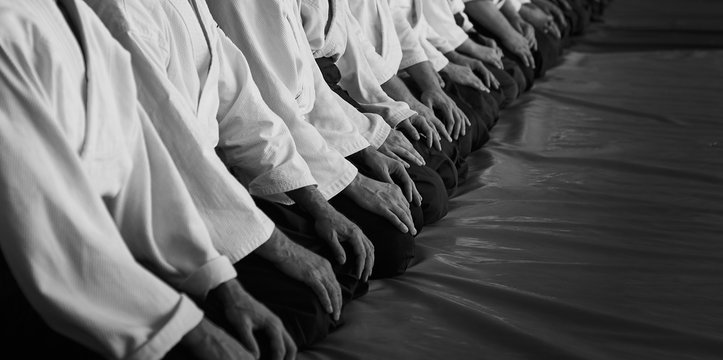 Black and white image of aikido. Men are sporsmen. Aikido workshop. A number of black belt practitioners in traditional uniform, white kimano and black hakama.