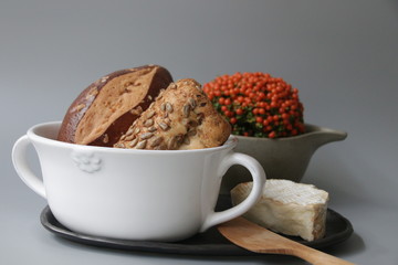 Breads in White Ceramic Bow and Traditional Cheese on Grey Background