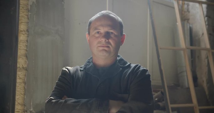 Middle-aged male professional carpentry master standing at wood manufacture with crossed arms being calm.