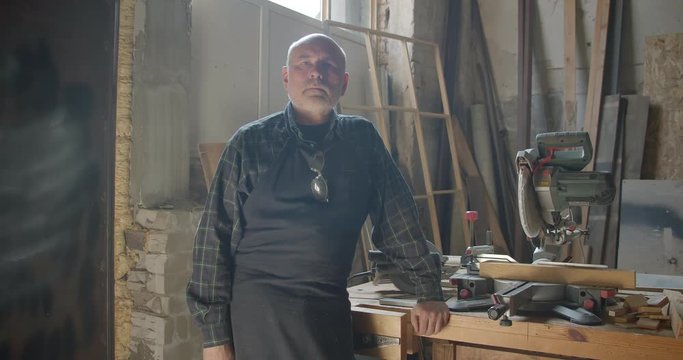 Senior gray haired male professional carpentry master standing at wood manufacture with crossed arms being calm.
