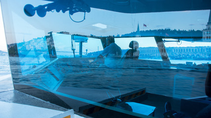the captain controls the boat along the Bosphorus, the surrounding water and buildings are reflected in the glass