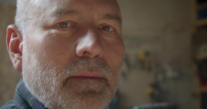 Close-up portrait of senior carpenter at wood manufacture watching into camera being serious and calm.