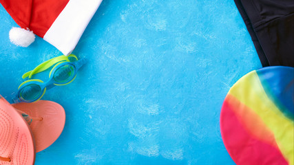 Christmas background for pool or fitness club. Santa Claus hat with swimming goggles, swimming trunks and flip-flops, as well as a swimming cap. happy new year 