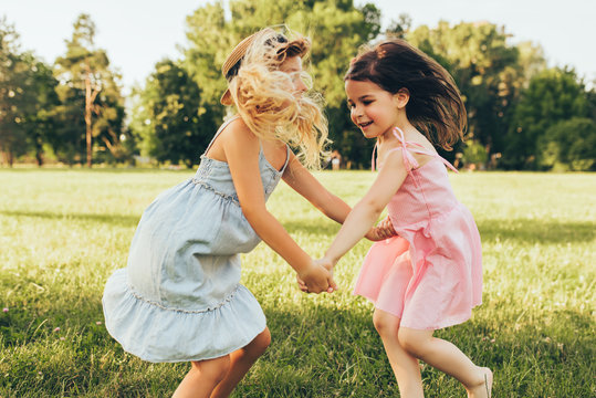 Image of two little girls dancing and playing together on the green grass in the park. Children enjoying summer days in the park. Two sisters having fun on nature background. Childhood and friendship