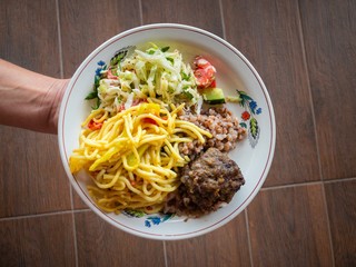 Hand taking plate full of food - vegetable salad, buckwheat, spaghetti, cutlet