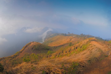 Mountain view of tourists standing on top hill around with mountains, soft mist with cloudy sky background, Phu Chi Fa (Phu Chee Fah), Chiang Rai, northern of Thailand.