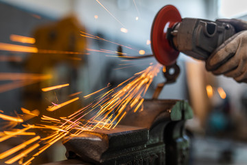 Worker cutting, grinding and polishing metal part with sparks indoor workshop, close-up.