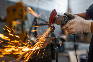 Worker cutting, grinding and polishing metal part with sparks indoor workshop, close-up.
