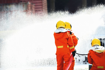 Three firefighters water spray with high pressure to fire surround with water drops and smoke.