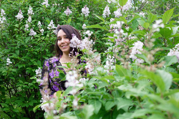 Portrait of beautiful young woman in black-purple dress in a garden with blooming lilac bushes.