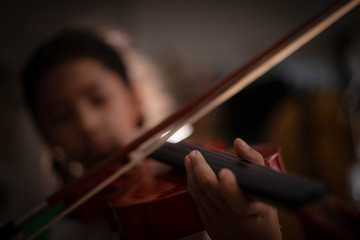 Close-up shot little girl playing violin orchestra instrumental with vintage tone and lighting effect dark and grain processed select focus shallow depth of field