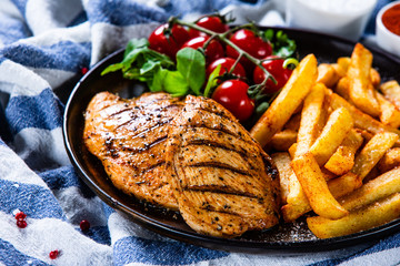 Grilled chicken fillet with french fries on wooden table