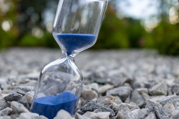 Hourglass with beautiful blue sand lie on small stones - obrazy, fototapety, plakaty