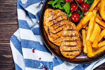 Grilled chicken fillet with french fries on wooden table