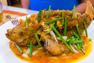 Whole fried fish on a plate with green onions in sauce