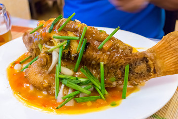 Fried fish in sauce with green onion on a plate in a restaurant