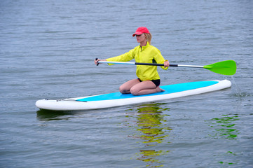 Beautiful young woman sitting on a board with a paddle