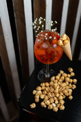 Sparkling light alcoholic cocktail with caramel popcorn, based on italian aperitif, apple cider, aperol and orange gin, served in blurred lights in a bar