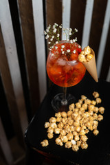Sparkling light alcoholic cocktail with caramel popcorn, based on italian aperitif, apple cider, aperol and orange gin, served in blurred lights in a bar