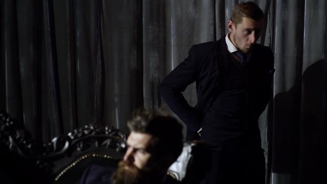 Buttoning a jacket. Stylish man in a suit fastening buttons on his jacket preparing for meeting. Two men in an expensive interior. Two business partners. Background. Rich background. Rich man.