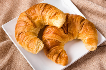 Croissants on a white plate on a linen tablecloth. Two croissants