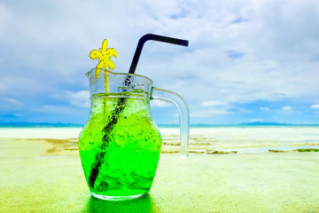 A glass of fresh green tropical fruit juice on the beach, on the table, against the sea 