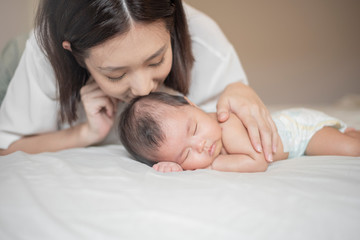 Beautiful mother is playing with her newborn baby in the bedroom.