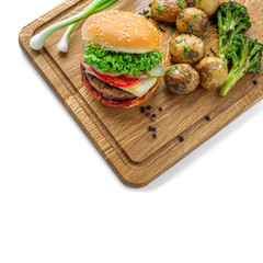 Delicious cheeseburger with baked potatoes, broccoli and scallion on a cutting board isolated on white background. Top view, shot from above.