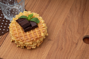 Belgian waffles with chunks on chocolate. Empty glass tumbler on a polka dot brown napkin