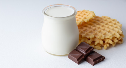 Crispy Belgian waffles with chocolate chips on a white textured surface. Small glass jug with milk