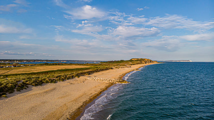An aerial view of a beautiful sandy beach along blue water sea and amaizing cliffs in the background at golden hour under a majestic blue sky and white clouds