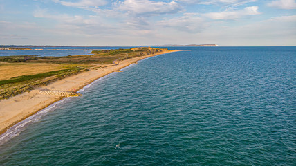 An aerial view of a beautiful sandy beach along blue water sea and amaizing cliffs in the background at golden hour under a majestic blue sky and white clouds
