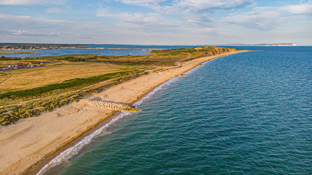 An aerial view of a beautiful sandy beach along blue water sea and amaizing cliffs in the background at golden hour under a majestic blue sky and white clouds