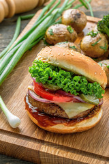 Classic hamburger with tomato, lettuce and onion served with grilled potatoes and broccoli on a wooden table.