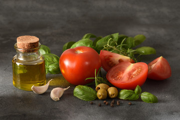 The ingredients for the salad with the tomatoes and olive oil on the dark background. The sliced ​​tomatoes