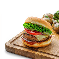 Delicious cheeseburger with baked potatoes, broccoli and scallion on a cutting board isolated on white background.