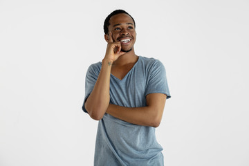 Beautiful male half-length portrait isolated on white studio background. Young emotional african-american man in blue shirt. Facial expression, human emotions, ad concept. Thinking, looking up.