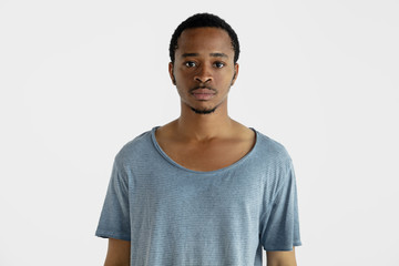 Beautiful male half-length portrait isolated on white studio background. Young emotional african-american man in blue shirt. Facial expression, human emotions, ad concept. Standing, looking at camera.