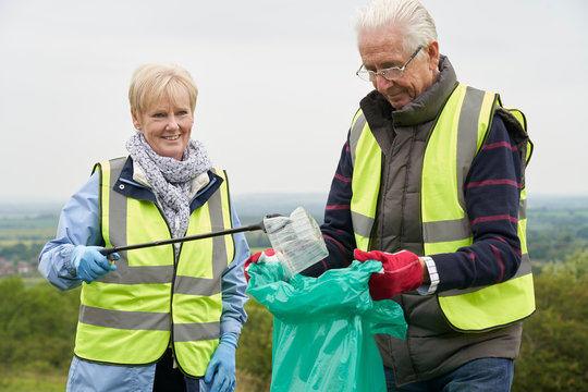 Helpful Senior Couple Collecting Litter In Countryside