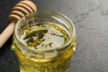 Flower organic honey in jar with wooden stick over black stone background. Copy space. Healthy food against flu. Homemade spa concept