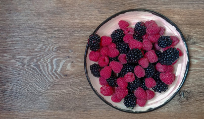 Mix of berries (blackberry and raspberry) on the plate on the wooden surface