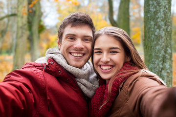 love, technology, relationship, family and people concept - happy smiling young couple taking selfie in autumn park