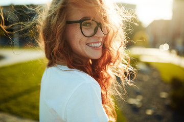 Portraits of a charming red-haired girl with a cute face. Girl posing for the camera in the city...