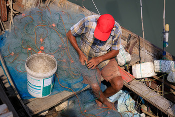 Fischer sitzt in einem Boot und repariert Fischernetze
